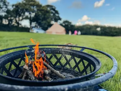 a fire pit with orange flames in a field at Furnished Bell Tent 3 in Carlyon Bay