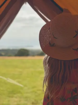 a woman wearing a hat looking out of a window at Furnished Bell Tent 3 in Carlyon Bay