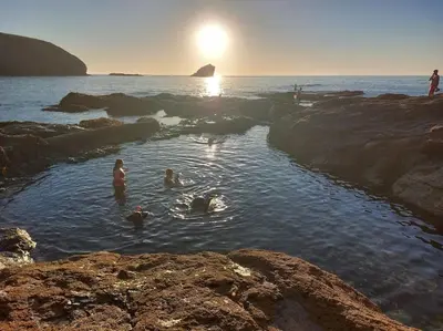 a group of people swimming in the water on the beach at The Cove, Portreath in Portreath