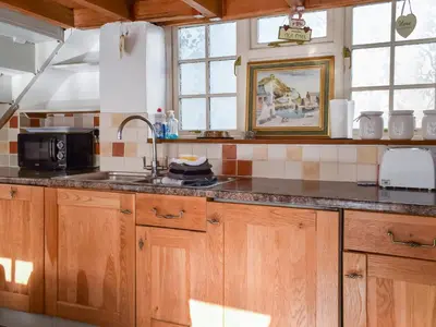 a kitchen with wooden cabinets and a sink with a microwave at Harbour Studio in Polperro
