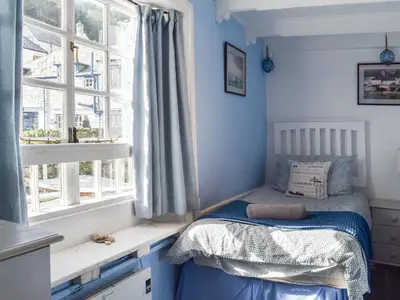 a small bedroom with a bed and two windows at Harbour Studio in Polperro