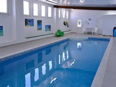a large swimming pool with blue water in a building at Eglos Derry Farm Cottage - E4597 in Cury