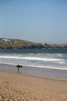 a person walking on the beach with a surfboard at Apartment Sea Views 5 mins Walk to Fistral in Newquay