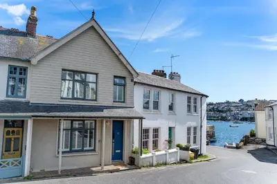 a white house with a blue door next to the water at Waterside cottage - log burner - 10 mins to Falmouth in Flushing