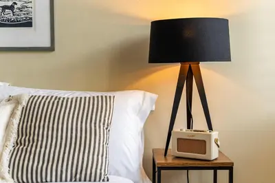a lamp on a table next to a bed with a clock at Waterside cottage - log burner - 10 mins to Falmouth in Flushing