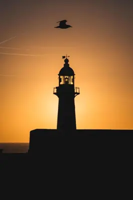 a lighthouse at sunset with a bird flying over it at Apartment Harbourside Hideaway by Interhome in Mevagissey