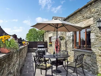a patio with a table and chairs and an umbrella at Bill And Ben's Cottage - Uk48619 in Warbstow