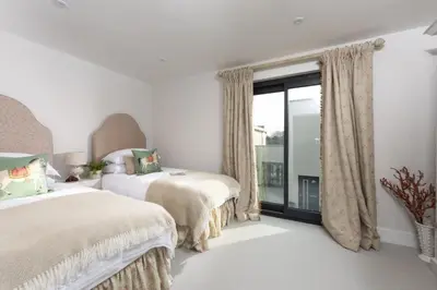 a white bedroom with two beds and a window at Harlyn Folly, Apartment 6, Harlyn in St Merryn