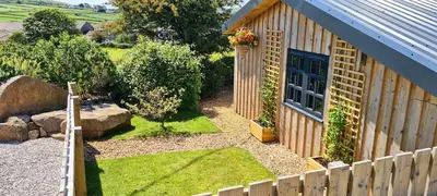 a garden next to a house with a fence at Honeysuckle Cabin in Redruth