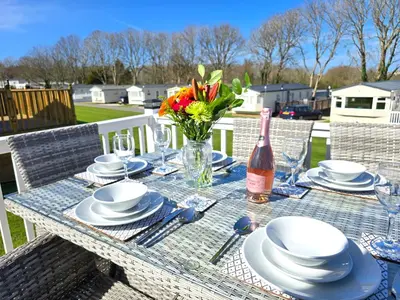 a table with plates and a bottle of wine and flowers at Cornwall Caravan Retreat 3 Crantock in Crantock