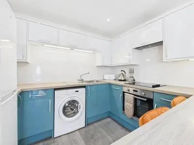 a kitchen with blue cabinets and a washer and dryer at Surf View by Signature Stays - Pool - Beach Access in Crantock