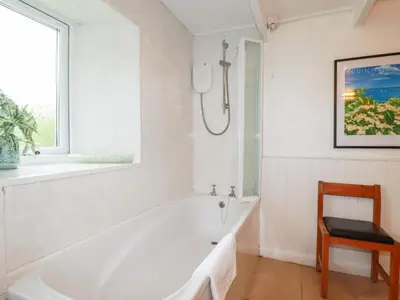 a white bathroom with a bath tub and a chair at Nanvivian in Feock