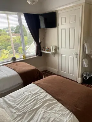 a bedroom with two beds and a window and a door at Cornerways Guest House St Austell Cornwall in St Austell