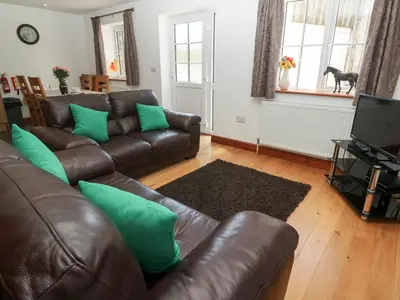 a living room with a brown leather couch and green pillows at The Stable Barn in Hayle