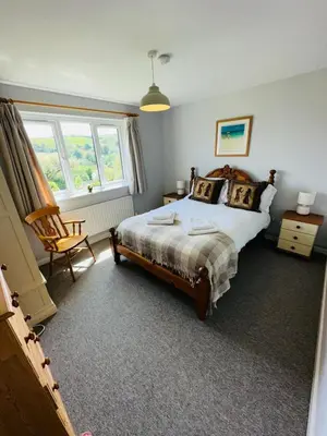 a bedroom with a bed and a chair and a window at Moogara in Gorran Haven