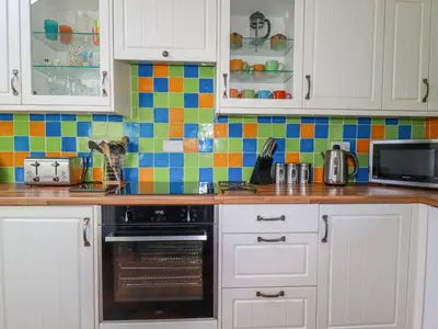 a kitchen with white cabinets and colorful tiles on the wall at The Old Piggery in Truro