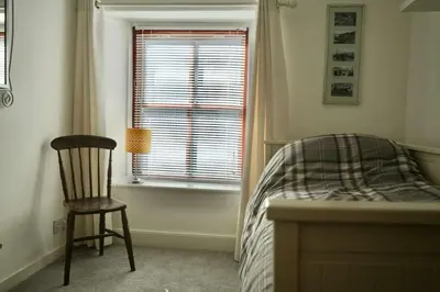 a bedroom with a bed and a chair and a window at Dunlin Cottage in Penryn