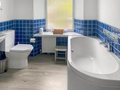 a bathroom with a tub and a toilet and blue tiles at Coastguards in Porthscatho