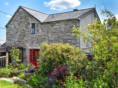 a stone house with a red door and some plants at Rivendell Cottage in Liskeard