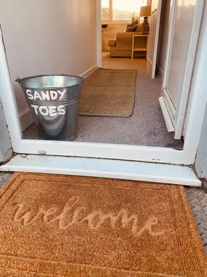 a door with a bucket in a hallway with the words sandy toes written on it at Lovely two bed flat with a sea view next to beach in Porthtowan