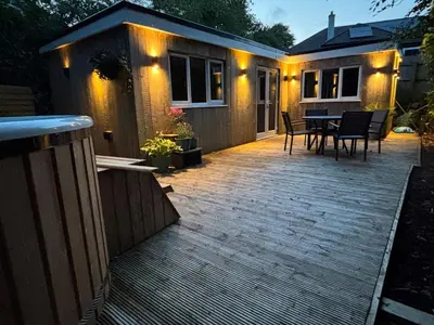 a backyard deck with a table and a house at Cornish wooden cabin & wood fired hot tub in Gwennap