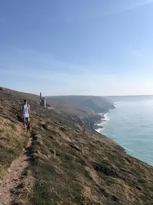 a man walking a dog on a hill next to the ocean at SeaNest, Aggie Home by the sea in St. Agnes