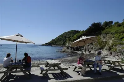 a group of people sitting at picnic tables on the beach at House 23 in Looe
