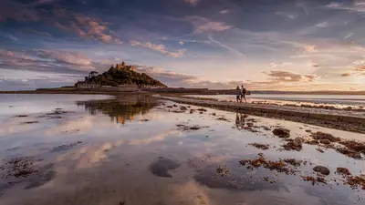 two people walking on the beach with a castle in the background at VITAMYN SEA, 4 bedroom house, Sleeps 8, 6 beds, Sea views, 5 min walk to harbour and beaches in St Ives