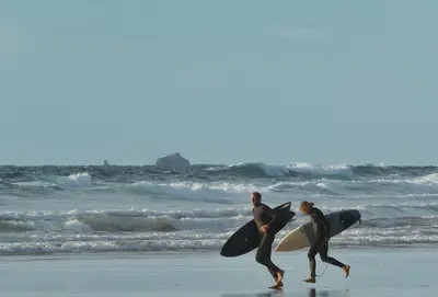 two men walking on the beach with their surfboards at Arnold Cottage in St Merryn