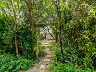 a path through a forest with a house in the background at On The Beach in Downderry