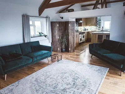 a living room with two green couches and a kitchen at The Retreat Cornwall holiday home with hot tub in Crowan