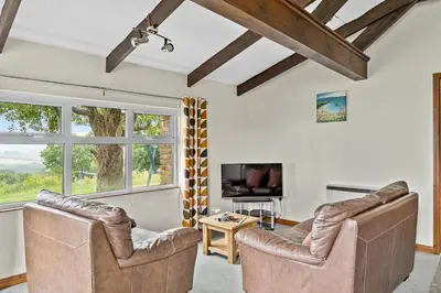 a living room with two leather chairs and a tv at Fuchsia Cottage in Saint Endellion
