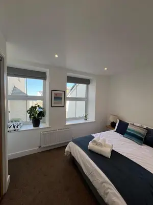 a bedroom with a large bed and two windows at 1 Bed Apartment in Town Centre in Newquay