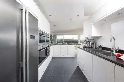 a kitchen with white cabinets and a stainless steel refrigerator at Ocean View, Mawgan Porth - Sea Views - Hot Tub - Free Parking & WiFi in Mawgan Porth
