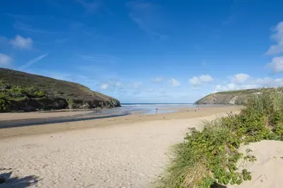 a sandy beach with people in the water at Ocean View, Mawgan Porth - Sea Views - Hot Tub - Free Parking & WiFi in Mawgan Porth