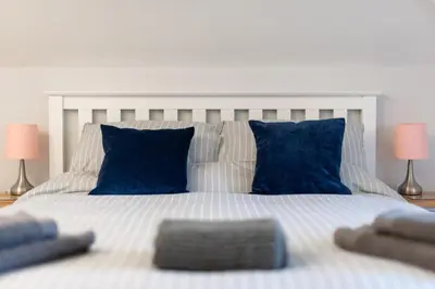 a large white bed with blue pillows and two lamps at Spacious Flat A Few Mins Walk to Carlyon Bay Beach in Carlyon Bay