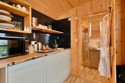 a kitchen with white cabinets and wooden walls at Finest Retreats - Demelza Shepherds Hut in Grade