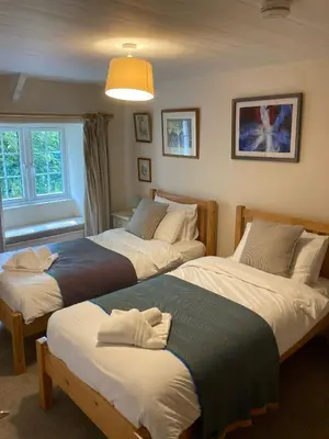 a bedroom with two beds and a window at Hollyhocks Cottage surrounded by beautiful Cornish countryside. in Helland