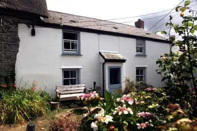 a white house with a bench in front of it at Crotchet Cottage near sandy beach at Porthbeor in Saint Anthony