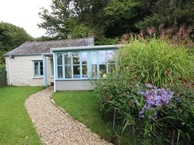 a small house with a greenhouse in a garden at Tinners Forge a pretty cottage near Mevagissey in St Austell