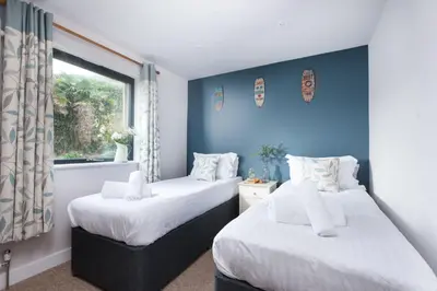 two beds in a room with blue walls and a window at Little Beachside in Newquay