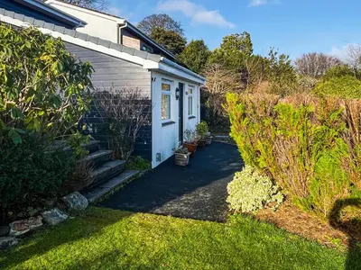 a garden with a small white house and some bushes at Hillside in St Austell