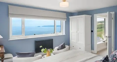 a bedroom with a bed and two chairs and a window at Luxury seaside home - 5 mins walk to beach - hot tub in Downderry