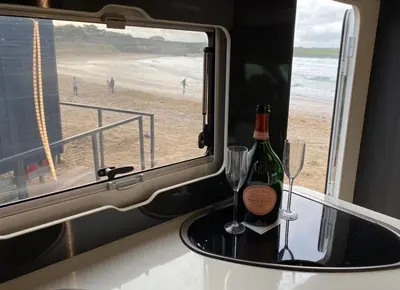 a bottle of wine and two glasses on a table near the beach at Raffy The Motorhome in St Merryn