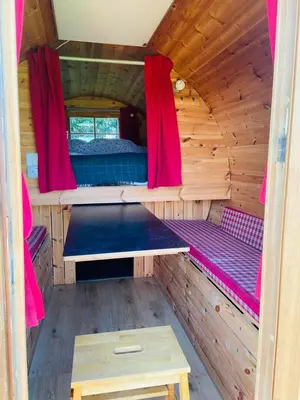 a inside of a wooden cabin with a bed and red curtains at Barrel Cabin 2 in Trethurgy
