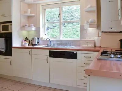 a kitchen with white cabinets and a sink and a window at Little Larnick in Looe