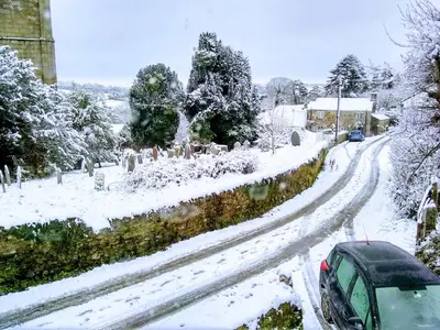a snow covered street with a car driving down a road at Tucked Away in Linkinhorne