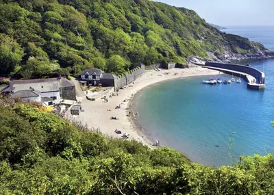 a beach with a group of people sitting on the beach at Talehay Cottages in Looe