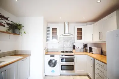a kitchen with white cabinets and a washer and dryer at Stunning Two Bed Sea View Apartment with Pool & Gym in Newquay