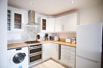a kitchen with white cabinets and a washer and dryer at Stunning Two Bed Sea View Apartment with Pool & Gym in Newquay